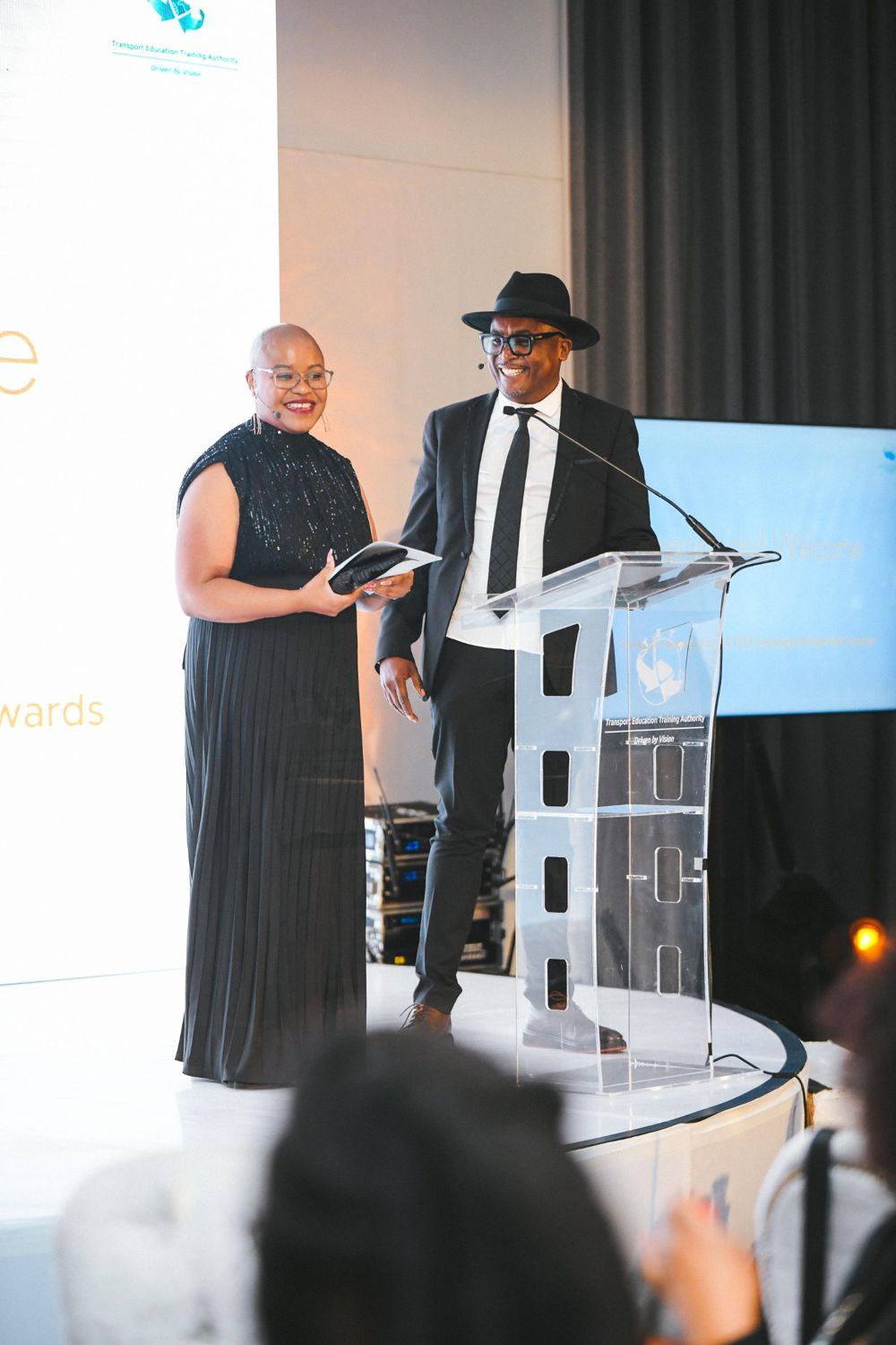 Two MCs smiling beside a perspex podium