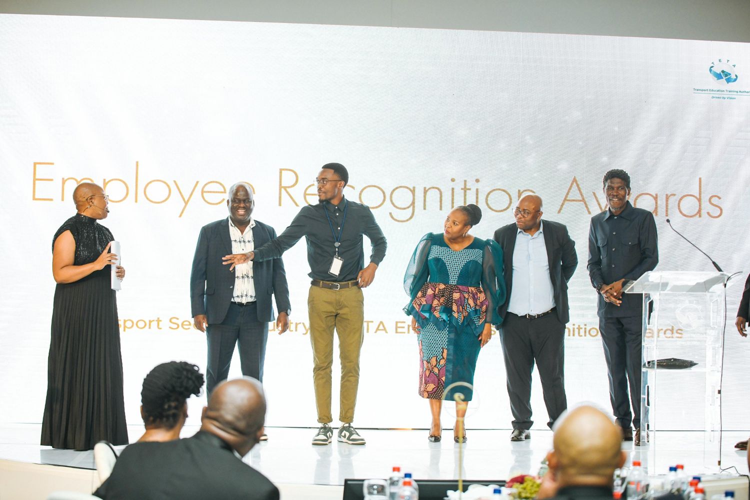 Wandii on stage with the MC and executives under the Employee Recognition Awards slide