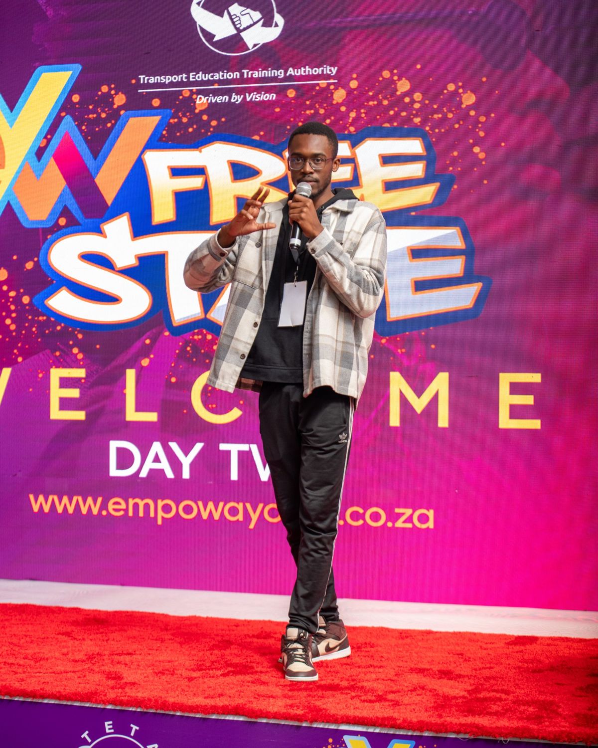 Wandii speaking into a microphone on stage at Empowa Youth Week Free State